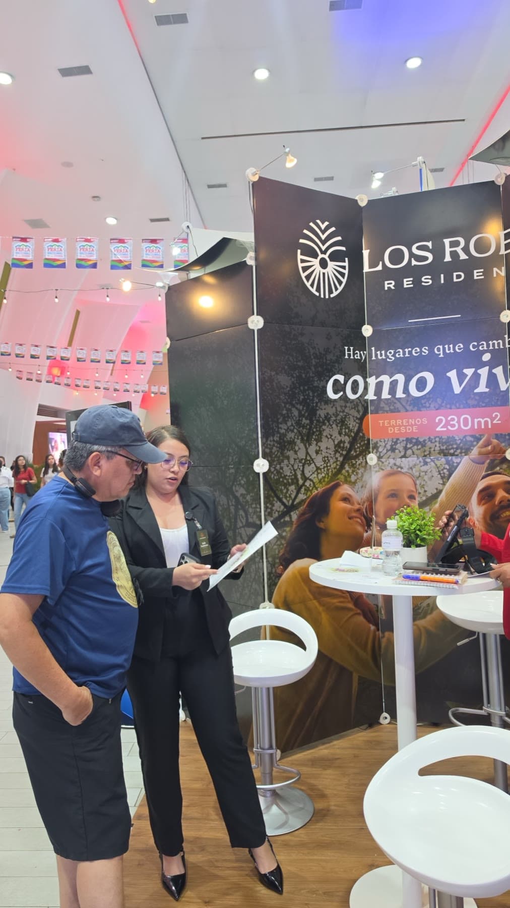 Dos visitantes revisan el material informativo frente al mural de Los Robles Residencial