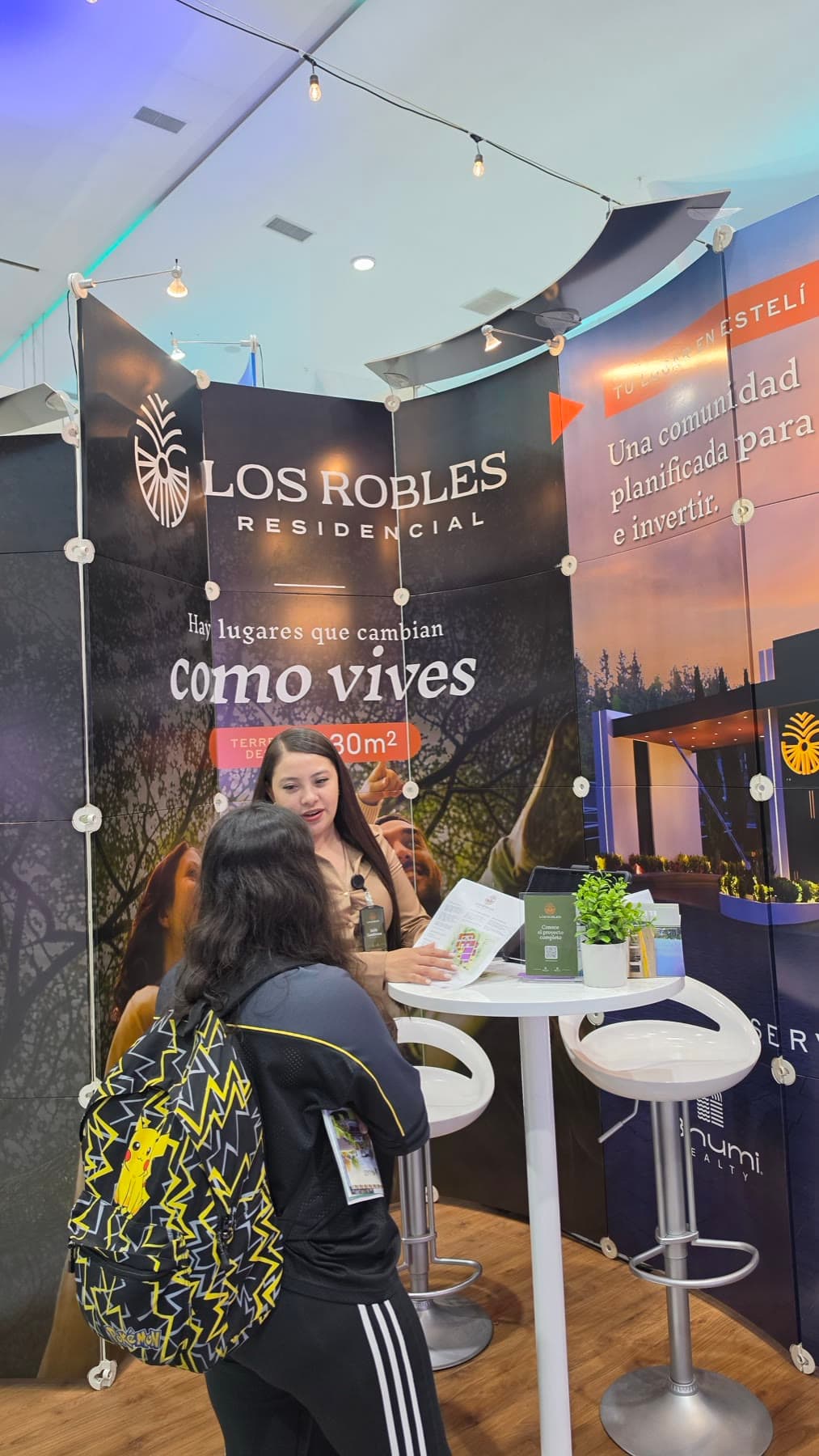 Una asesora explica el plano de lotes a una visitante en el stand